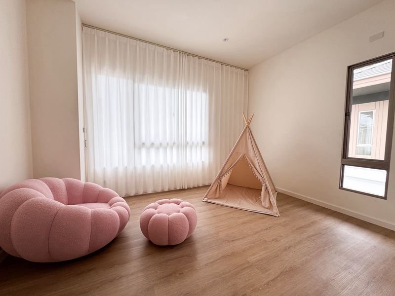Bright minimalist playroom with a large pink tufted circular chair, a matching pink pouf, and a pink fabric teepee on a wood floor near a window.