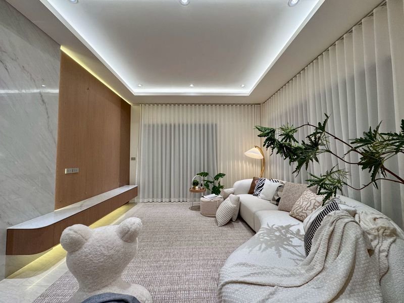 Bright modern living room with a white sectional plush cushions and large indoor plants under a recessed ceilinghttps