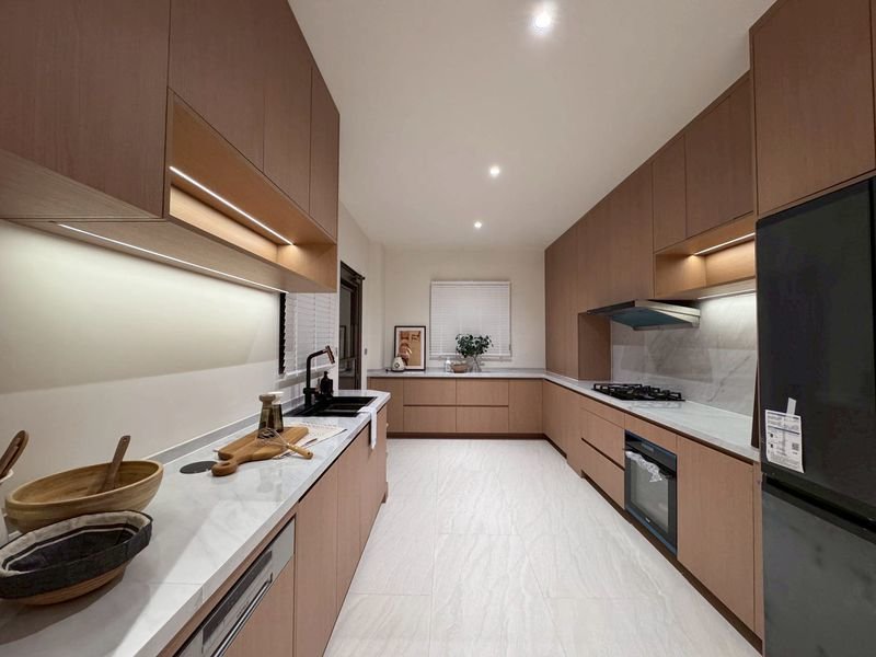 Bright L-shaped kitchen with light wood cabinets, white countertops, and a gas cooktop under a range hood.