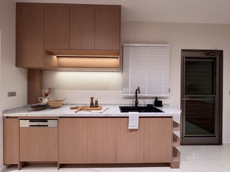 Modern kitchen with light wood cabinets, white countertop, and a black sink under a window with blinds.