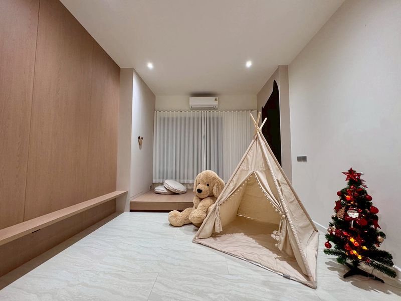 Beige children's tent set up in a modern living room with a large teddy bear and a small decorated Christmas tree nearby.