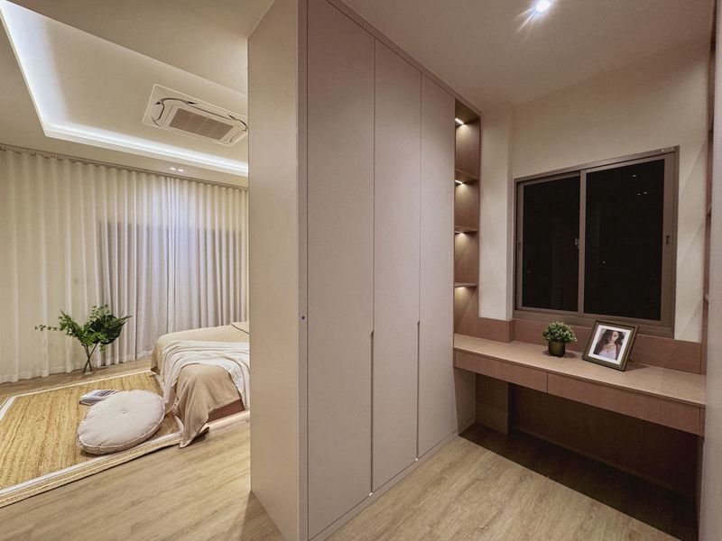Modern bedroom with a tall built-in wardrobe separating the sleeping area from a desk by the window, plus a plant and photo frame on the desk.