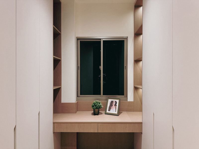 Wooden desk area between tall cabinets with a window, featuring a small potted plant and a framed photo on the surface at night.