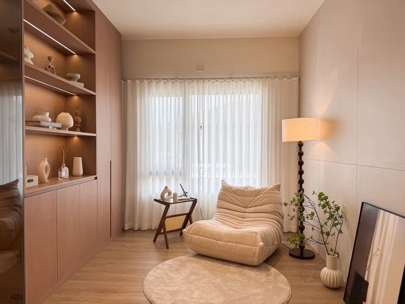 Neutral living room with a beige bean bag chair, round rug, and built-in wooden shelves on the left.