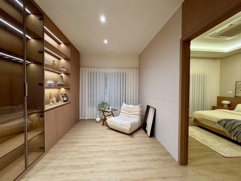 Modern living area with built-in wooden cabinets on the left, a white cushioned chair, small table, and a plant.