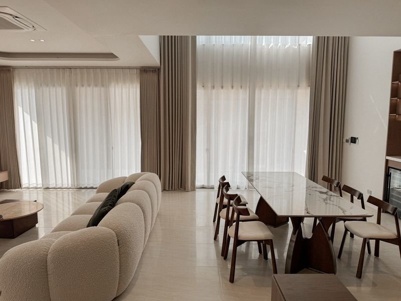 Modern living and dining space with a curved beige sofa and a marble dining table.