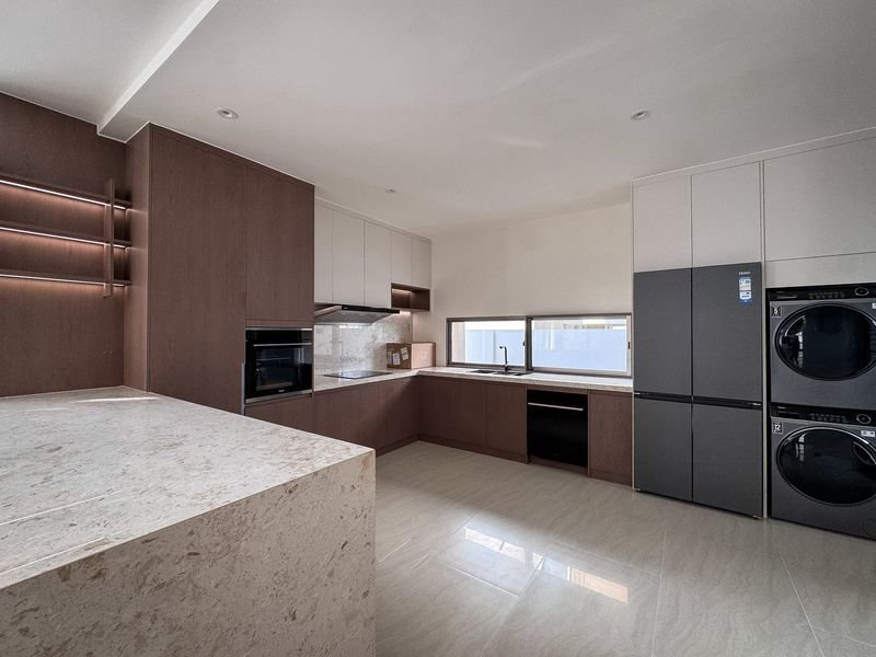 Modern L-shaped kitchen with dark wood cabinets, light countertops, and a large island; stainless appliances including a double fridge and stacked washer/dryer.