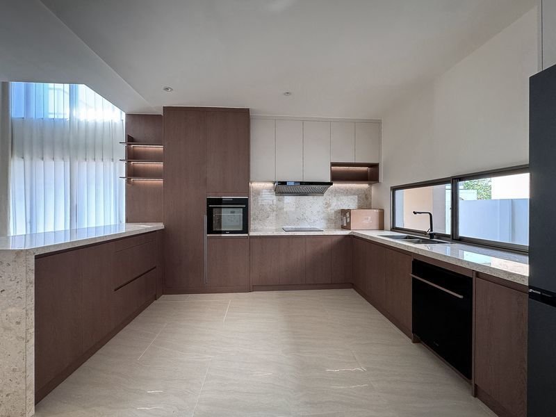 Modern L-shaped kitchen with dark wood lower cabinets, white uppers, built-in oven, range hood, and marble countertops by a large window.