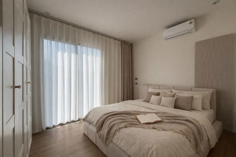 Bright modern bedroom with a large bed, neutral linens, and sheer curtains along floor-to-ceiling windows.