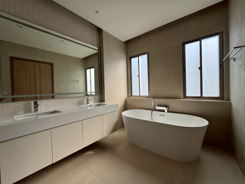 Modern bathroom with a freestanding oval tub by two tall windows and a white double-sink vanity under a large mirror.