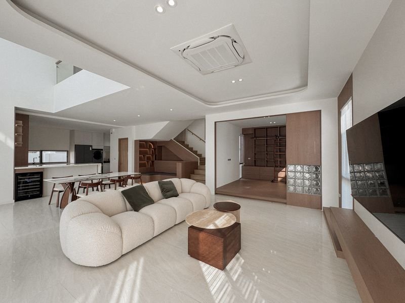 Open-concept living room with a curved cream sofa, round wooden coffee tables, and a wall-mounted TV area to the right.
