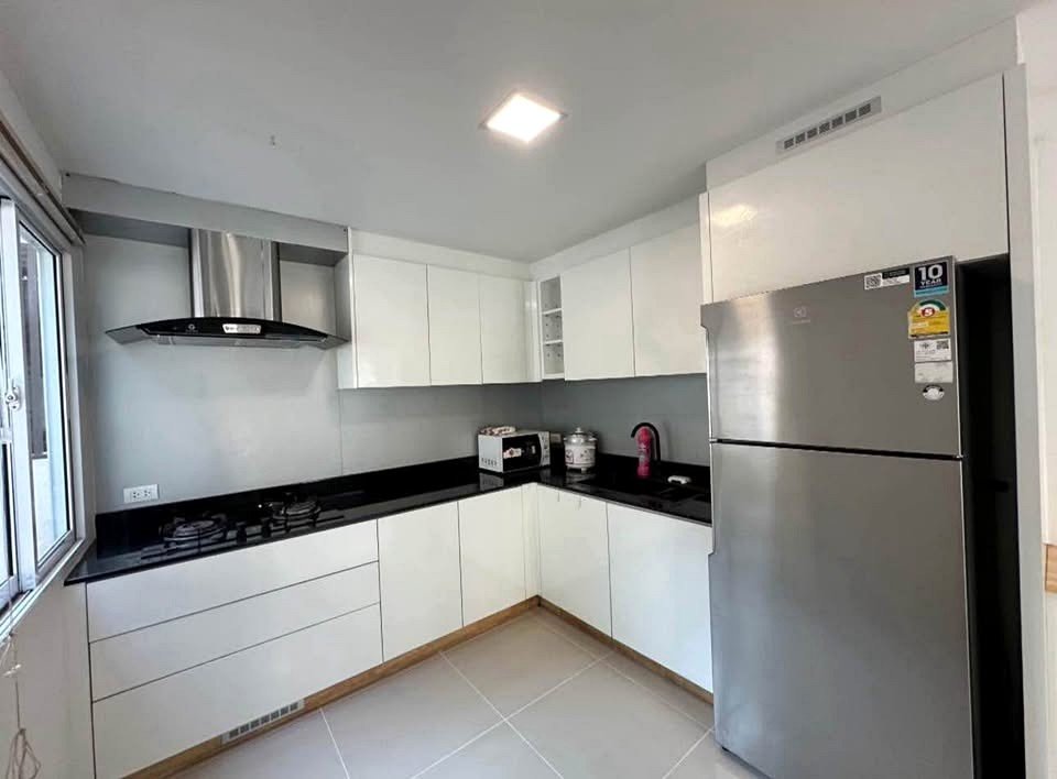 Modern L-shaped kitchen with white cabinets, black countertop, stainless steel fridge, gas stove, and range hood.