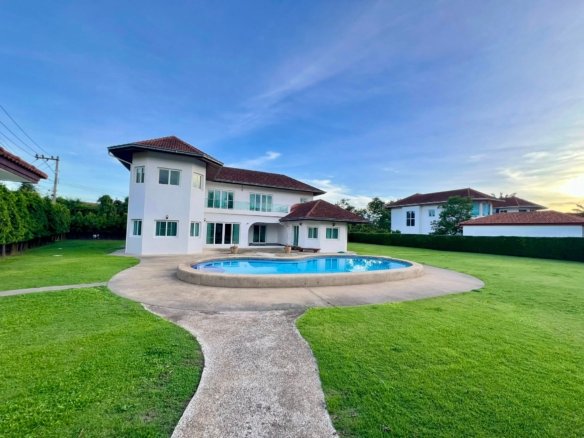 Modern white two story house with a red tiled roof large windows and a circular in ground pool in the lawn beneath a clear blue sky