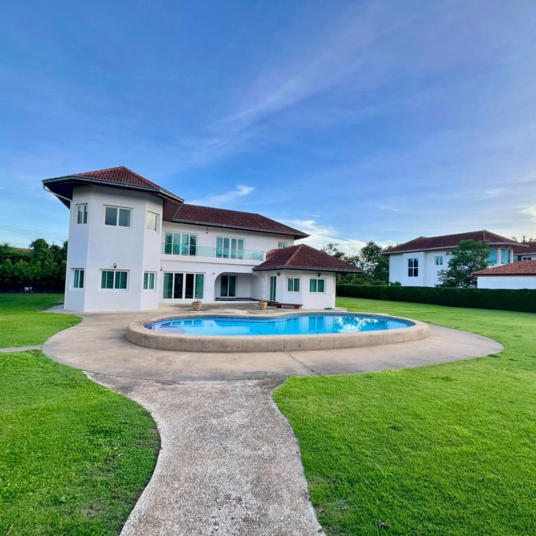 Modern white two story house with a red tiled roof large windows and a circular in ground pool in the lawn beneath a clear blue sky