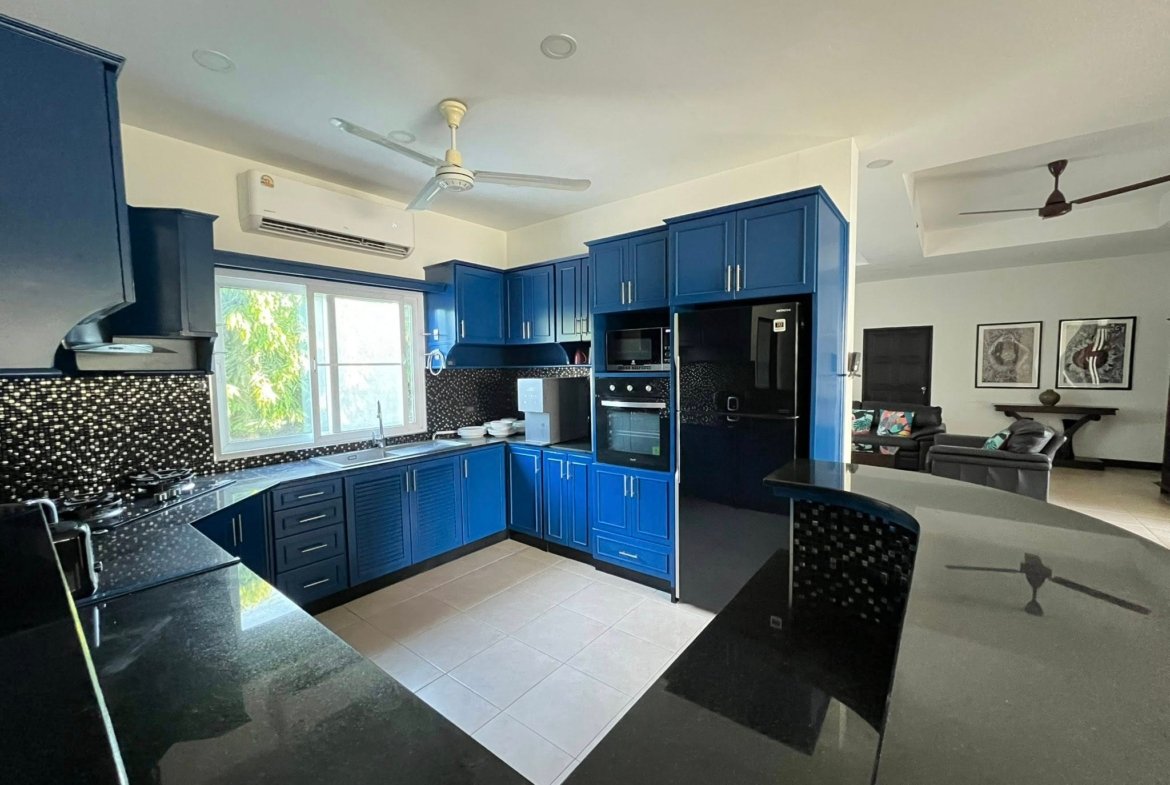 Modern kitchen with blue cabinets, black granite countertops, and stainless steel appliances under a white ceiling fan.