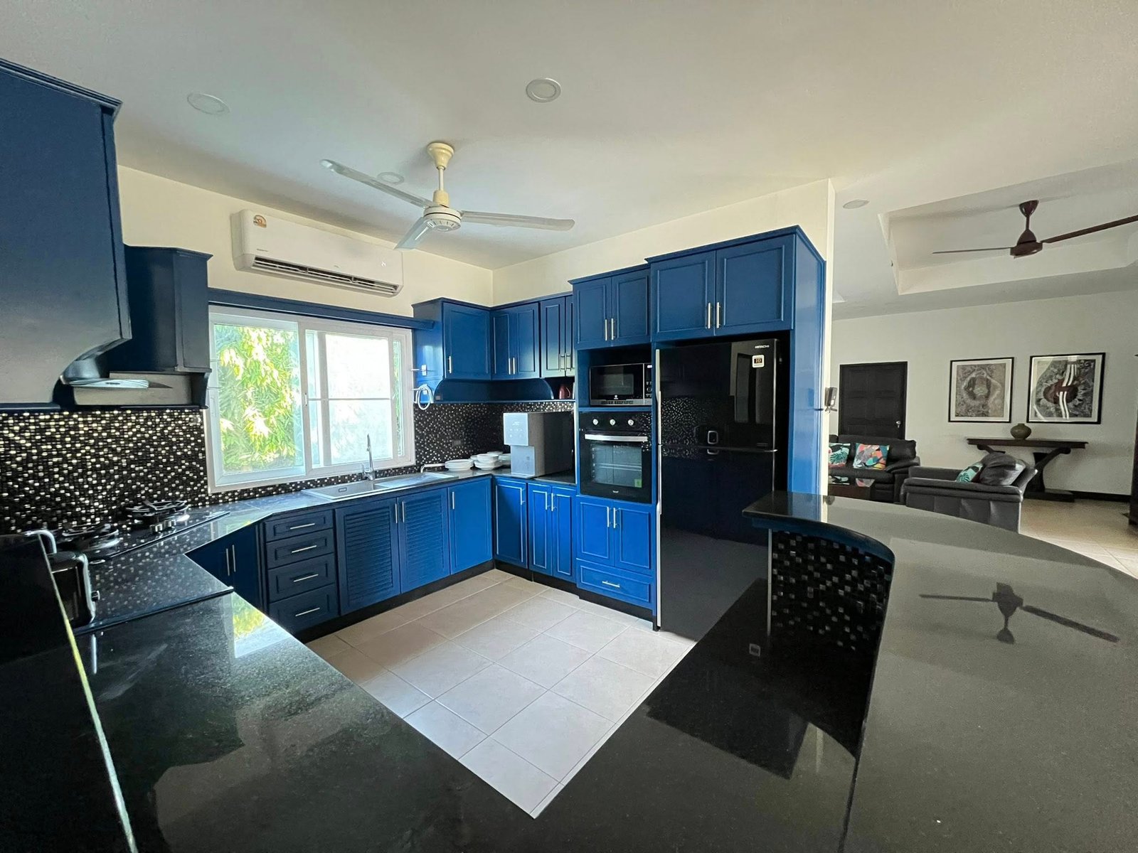 House_Sale_Mabprachan_Pattaya_Dlh533_12 Modern kitchen with blue cabinets, black granite countertops, and stainless steel appliances under a white ceiling fan.