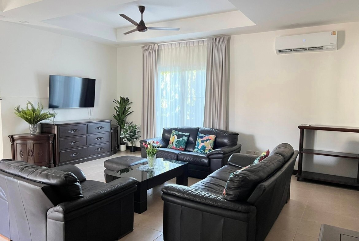 Living room with black leather sectional, wall-mounted TV on a dark dresser, and potted plants.