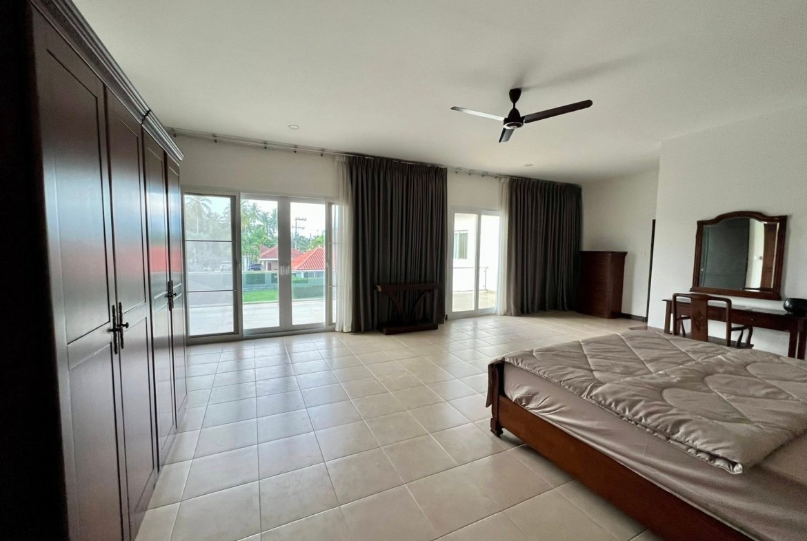 Spacious bedroom with dark wooden wardrobes along the left, tiled floor, and a ceiling fan above.