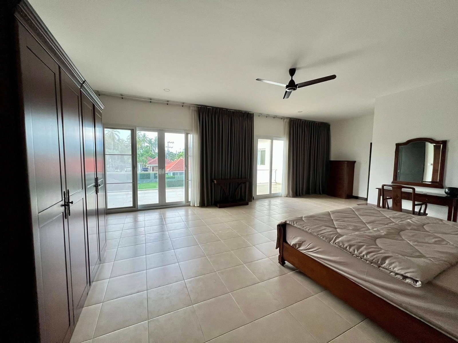 House_Sale_Mabprachan_Pattaya_Dlh533_16 Spacious bedroom with dark wooden wardrobes along the left, tiled floor, and a ceiling fan above.