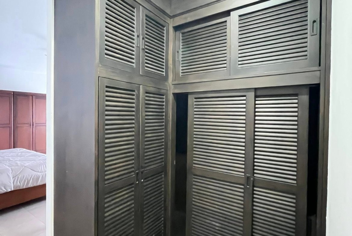 Dark gray corner wardrobe with louvered doors occupying most of the wall, next to a bed in a bedroom.