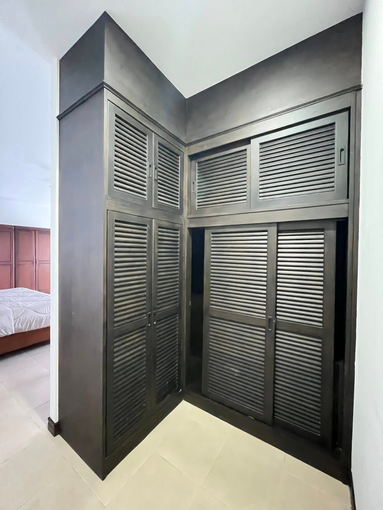 House_Sale_Mabprachan_Pattaya_Dlh533_18 Dark gray corner wardrobe with louvered doors occupying most of the wall, next to a bed in a bedroom.