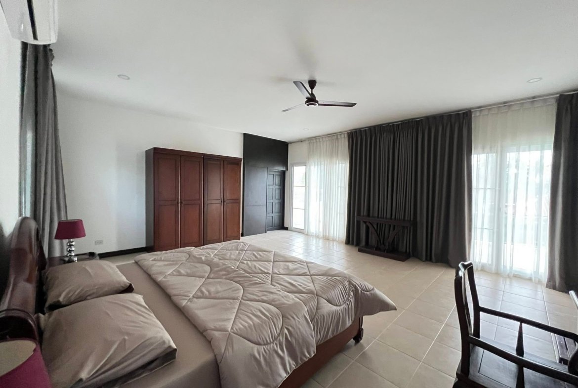 Spacious bedroom with two large beds, dark wood wardrobe, and ceiling fan in a bright, modern room.