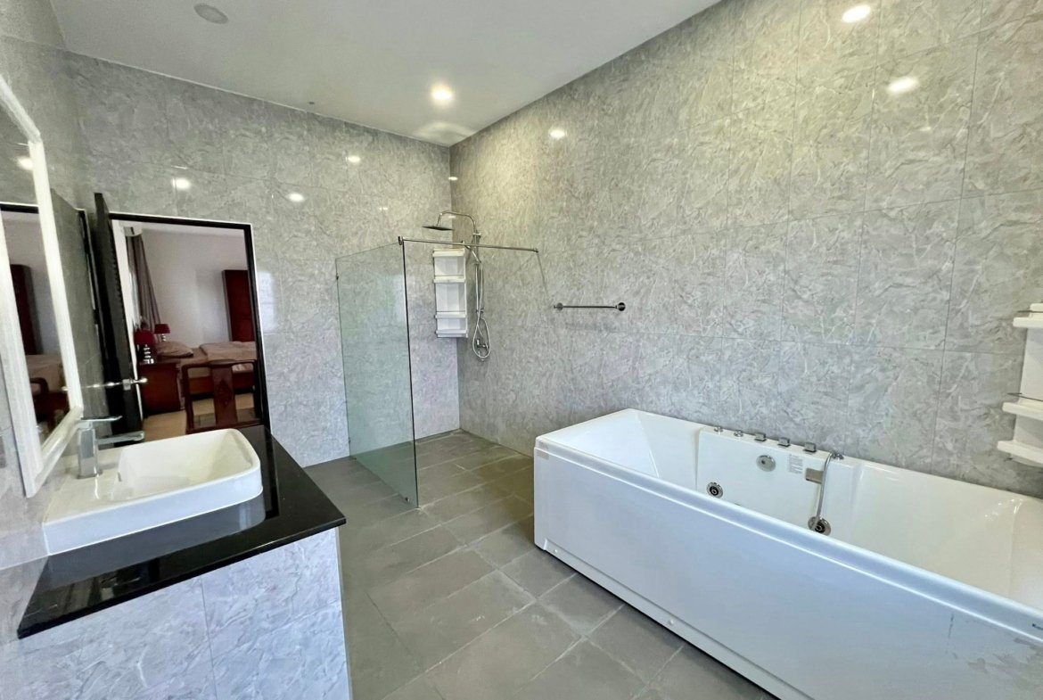 Modern bathroom with grey marble walls, glass shower enclosure, and white bathtub.