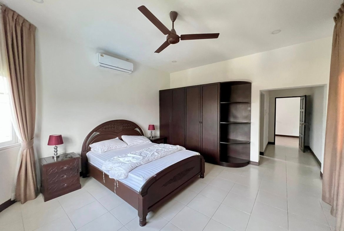 Dark wood bedroom with a large bed, matching nightstands, built-in wardrobe, white bedding, and a ceiling fan.