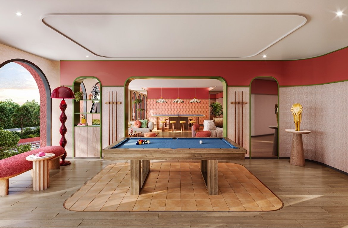 A bright game room with a blue pool table at the center, wood furniture, and pink-red walls with rounded arches framing a lounge area beyond.