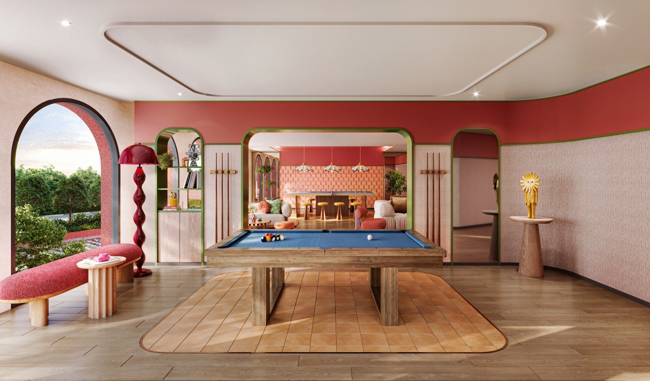 INY_LOUNGE_FINAL A bright game room with a blue pool table at the center, wood furniture, and pink-red walls with rounded arches framing a lounge area beyond.
