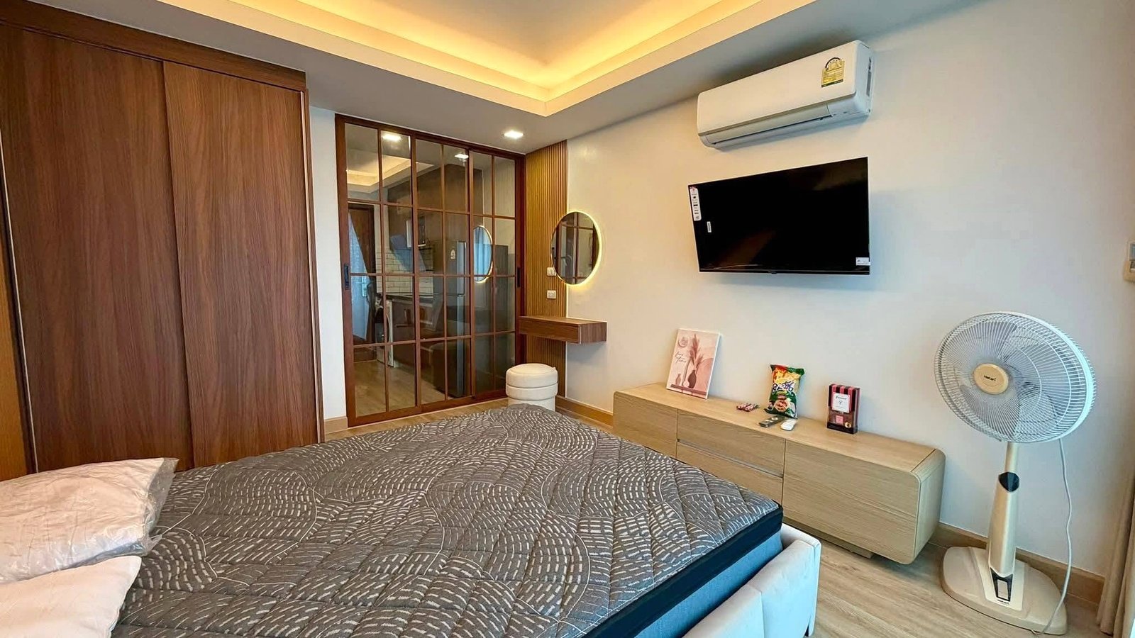 LBR2_Pattaya_Sale_Dlc613_7 Bedroom with a large wooden wardrobe, glass sliding partition, and a bed with a gray patterned comforter in the foreground.