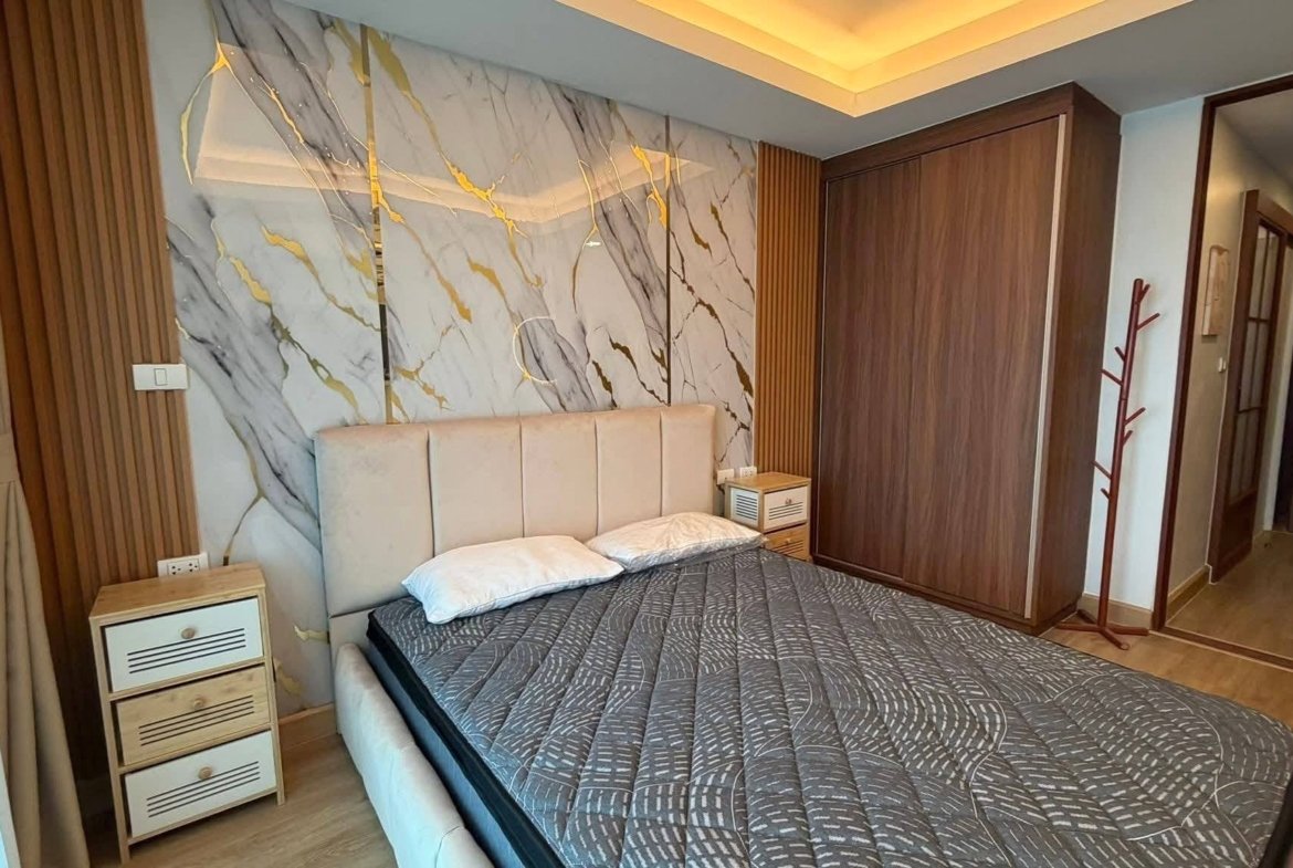 Bedroom with a marble accent wall, upholstered headboard, and two small wooden nightstands flanking the bed.