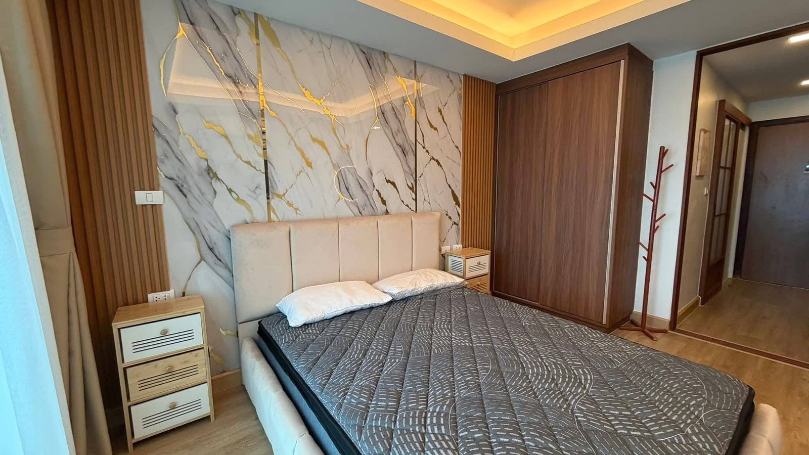 LBR2_Pattaya_Sale_Dlc613_8 Bedroom with a marble accent wall, upholstered headboard, and two small wooden nightstands flanking the bed.