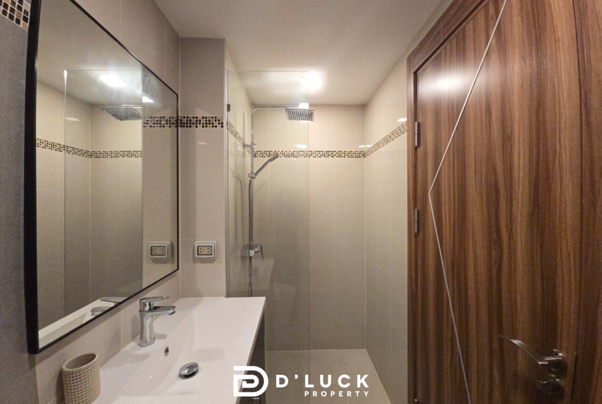 Modern bathroom with a white double sink, large wall mirror, glass shower, and mosaic tile accent strip.
