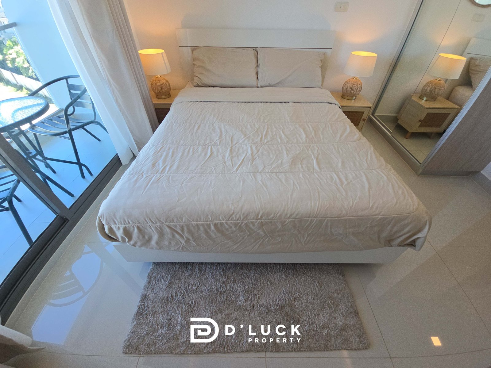 Bright, minimalist hotel bedroom with a white bed, two beige pillows, and wicker-lamp nightstands; glass balcony door on the left.