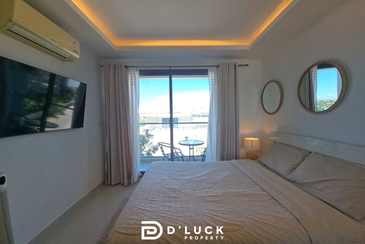 Hotel bedroom with two beds, balcony door, white curtains, and warm recessed ceiling lighting.