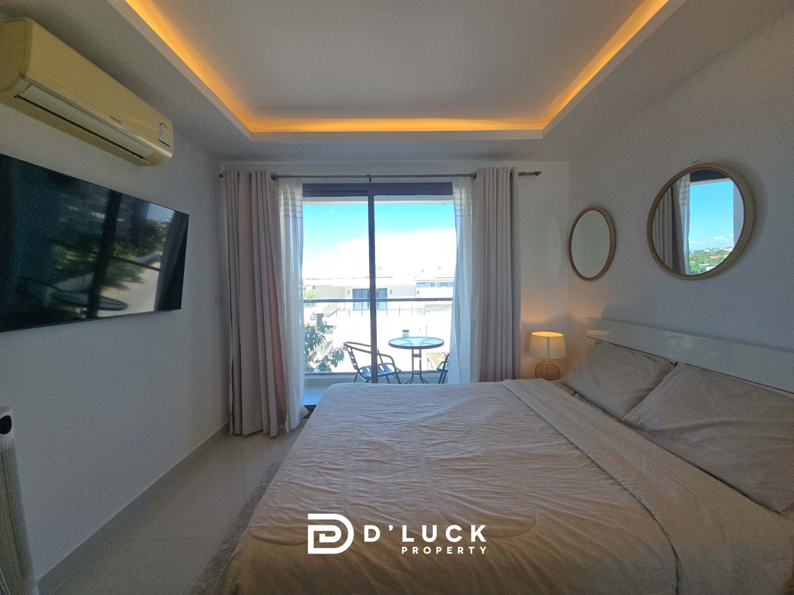 Hotel bedroom with two beds, balcony door, white curtains, and warm recessed ceiling lighting.