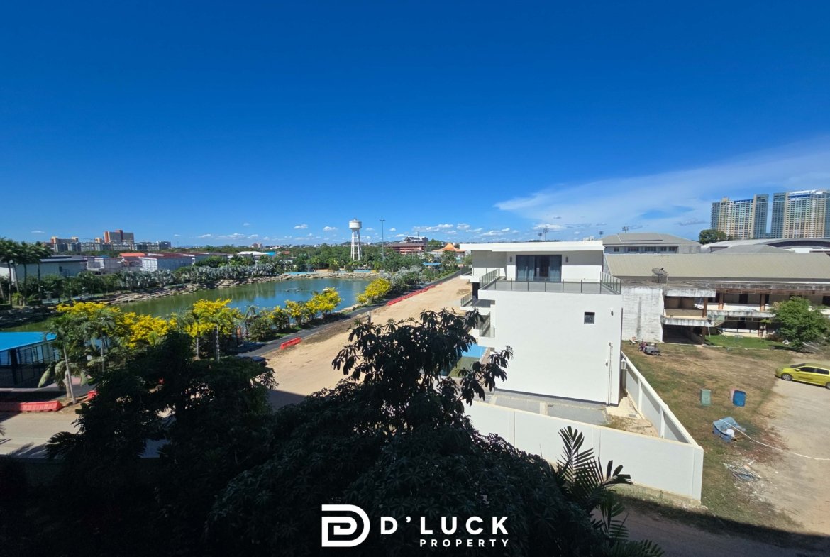 Wide daytime view of an urban landscape with a river, greenery, and a white modern building; D'Luck Property logo visible at the bottom.