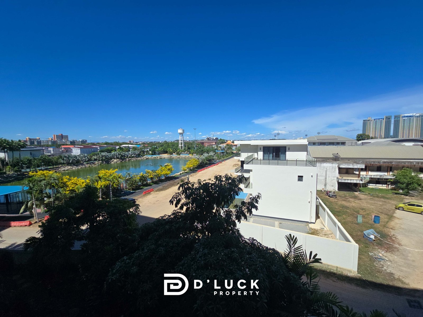 Wide daytime view of an urban landscape with a river, greenery, and a white modern building; D'Luck Property logo visible at the bottom.