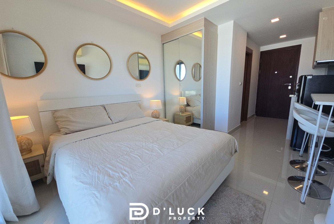 Hotel bedroom with two single beds pushed together, round wall mirrors, a mirrored wardrobe, and warm bedside lamps. A small dining bar area is visible in the foreground.