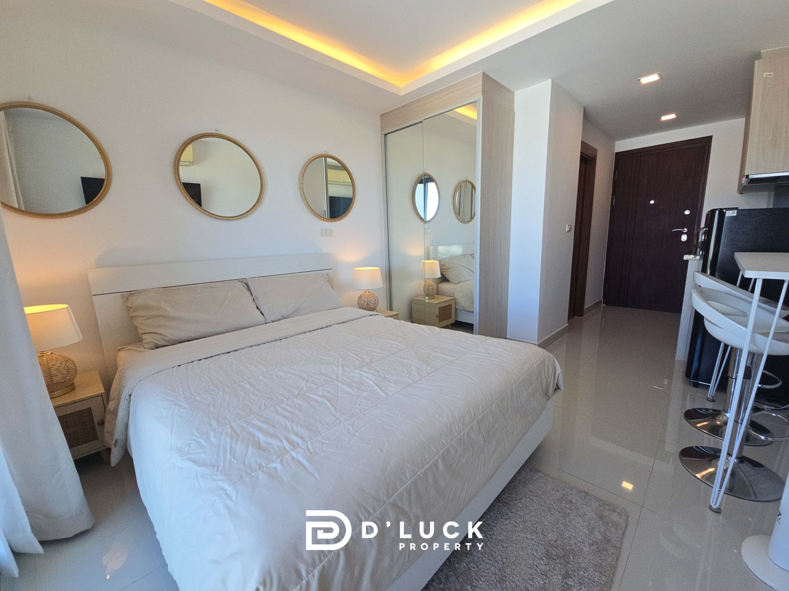 Hotel bedroom with two single beds pushed together, round wall mirrors, a mirrored wardrobe, and warm bedside lamps. A small dining bar area is visible in the foreground.