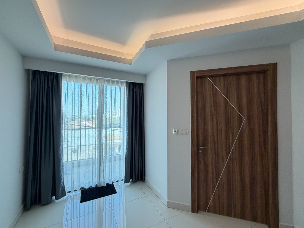 Bright modern room with a large window covered by sheer white and dark curtains, view of buildings outside.