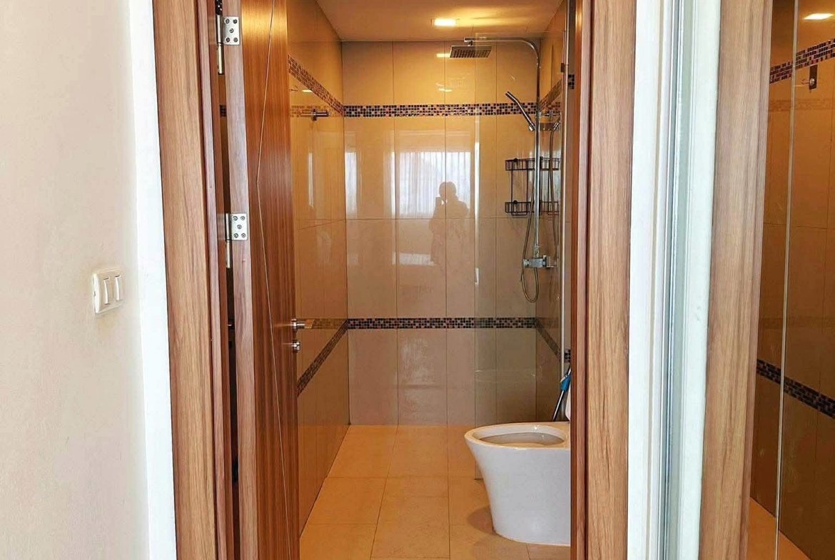 Open doorway into a beige-tiled bathroom with a glass shower enclosure and a white toilet at the entrance.