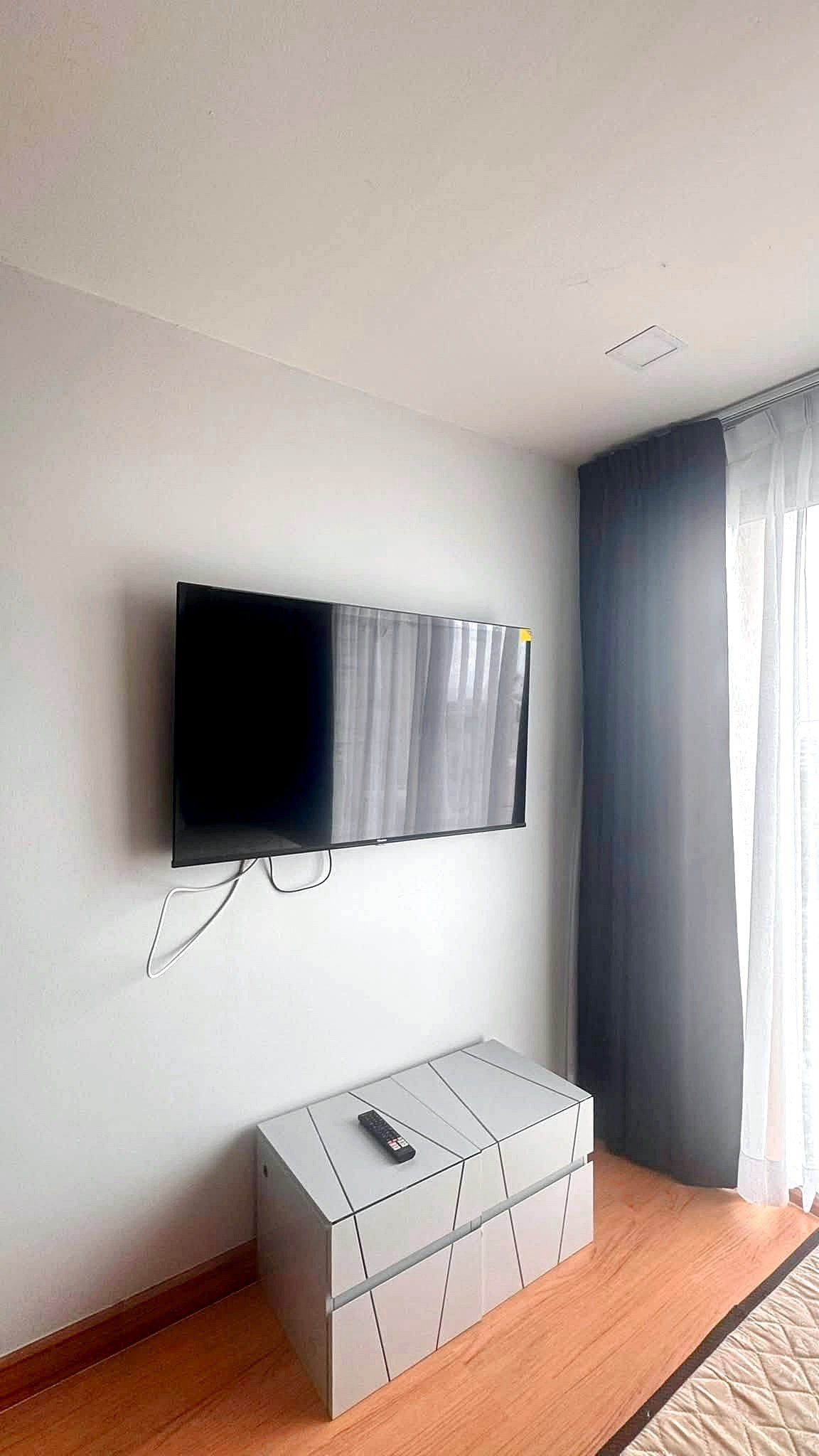 Laguna_2_Pattaya_Sale_Dlc644_11 Wall-mounted flat-screen TV above a white geometric cabinet, remote on top and visible cables in a bright living space.