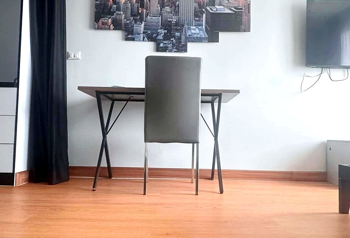 Desk and gray chair in a bright room with a multi-panel city skyline wall art, black curtain on the left, and a wall-mounted TV on the right.