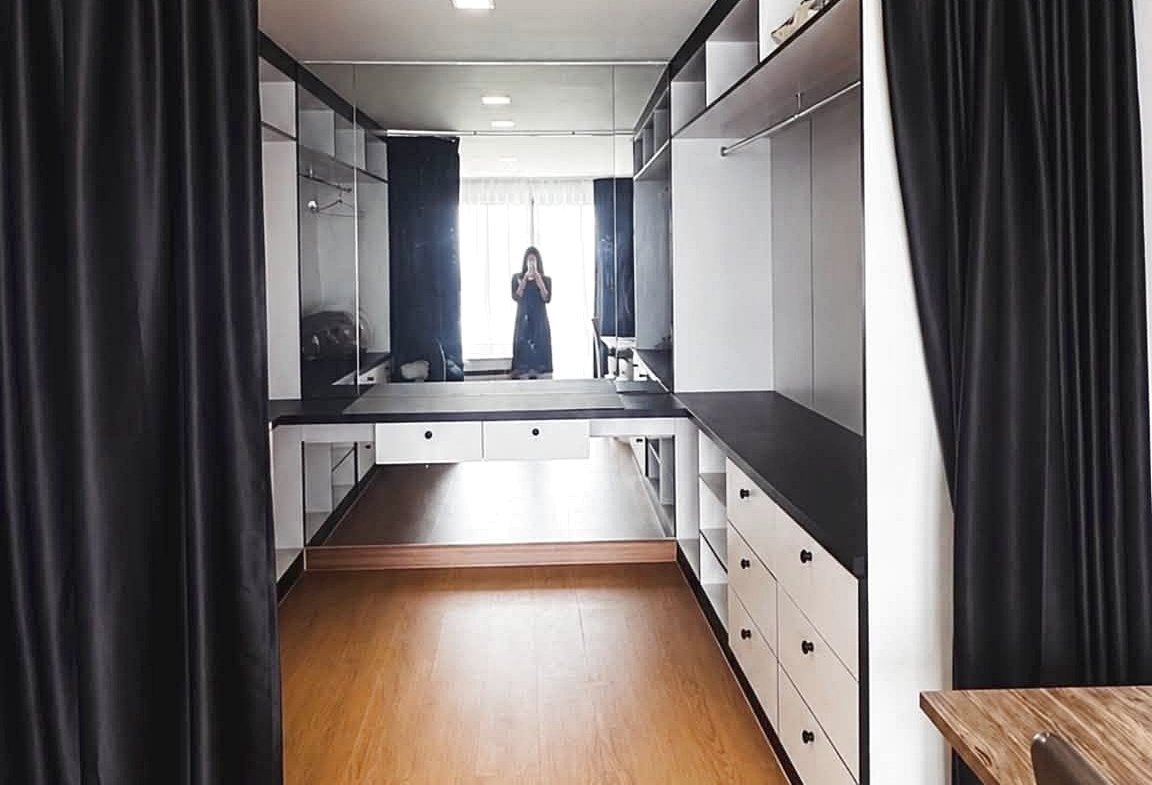 Long dressing room with wooden floor, black curtains, and a mirrored wall; a person is taking a photo in the distance.