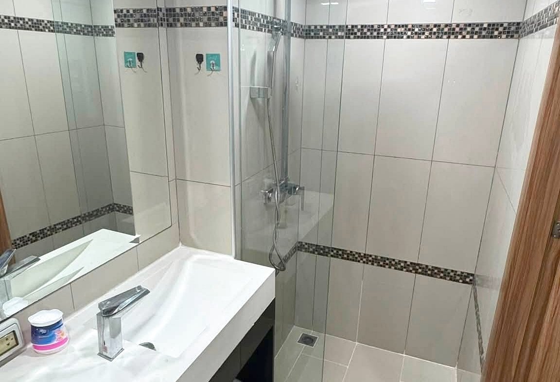 Modern bathroom with a glass shower enclosure, rainfall shower head, and a white sink on a dark vanity.