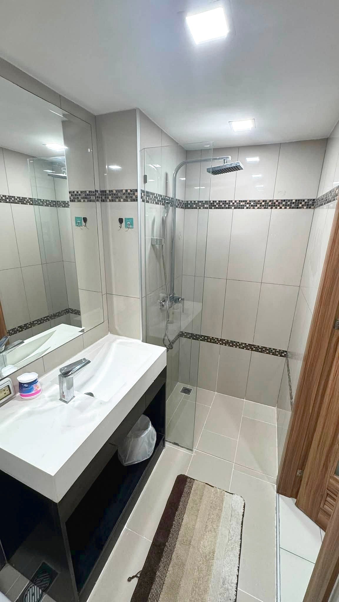 Modern bathroom with a glass shower enclosure, rainfall shower head, and a white sink on a dark vanity.