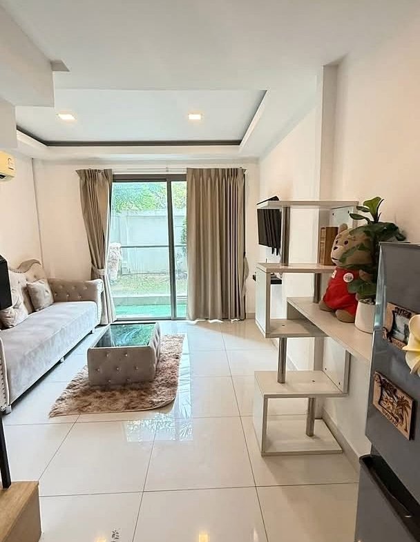 Bright living room with white tiled floor, beige sofa, glass coffee table on a shag rug, and sliding glass doors to a balcony.