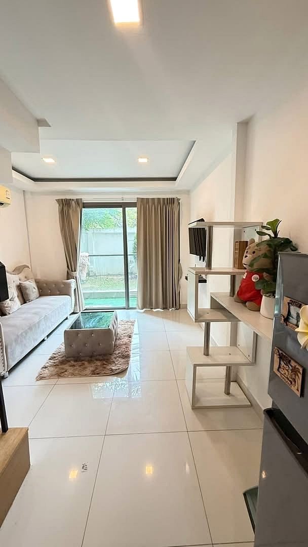 Laguna_Beach_2_Pattaya_Dlc627 Bright living room with white tiled floor, beige sofa, glass coffee table on a shag rug, and sliding glass doors to a balcony.